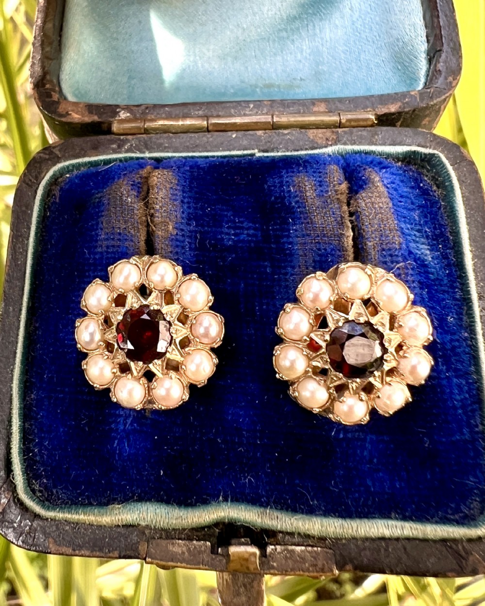 A pair of Victorian gold cluster earrings featuring a central round faceted red garnet surrounded by seed pearls set in a starburst pattern. View VII