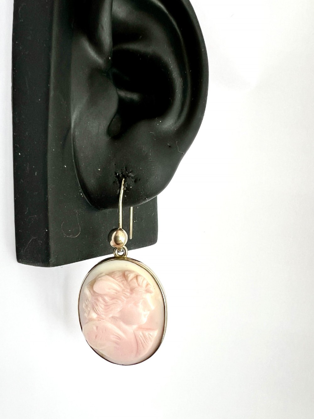 A pair of oval drop earrings featuring carved pink and white queen conch shell cameos depicting classical profile portraits set in silver mounts. View V