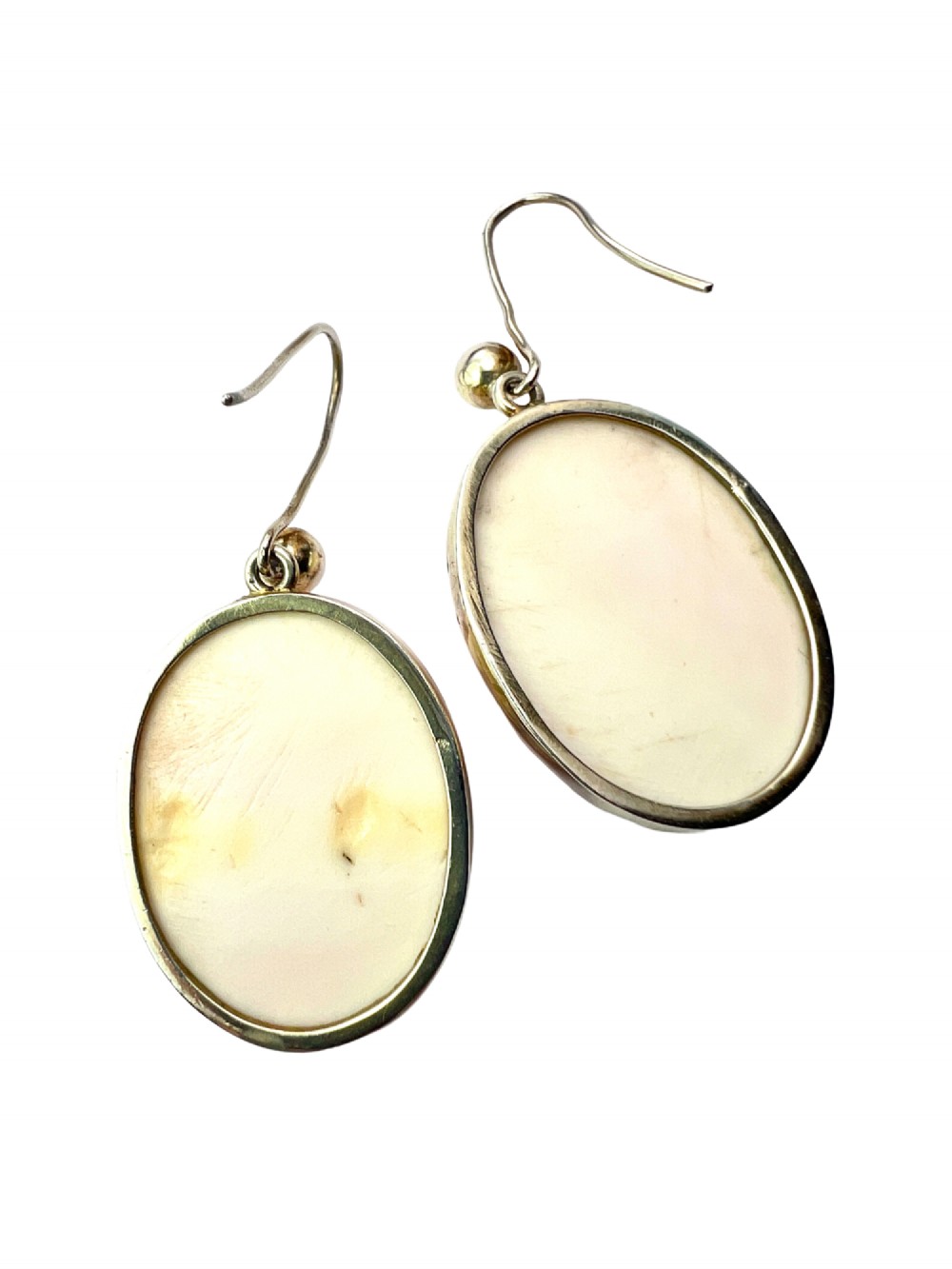 A pair of oval drop earrings featuring carved pink and white queen conch shell cameos depicting classical profile portraits set in silver mounts. View VI
