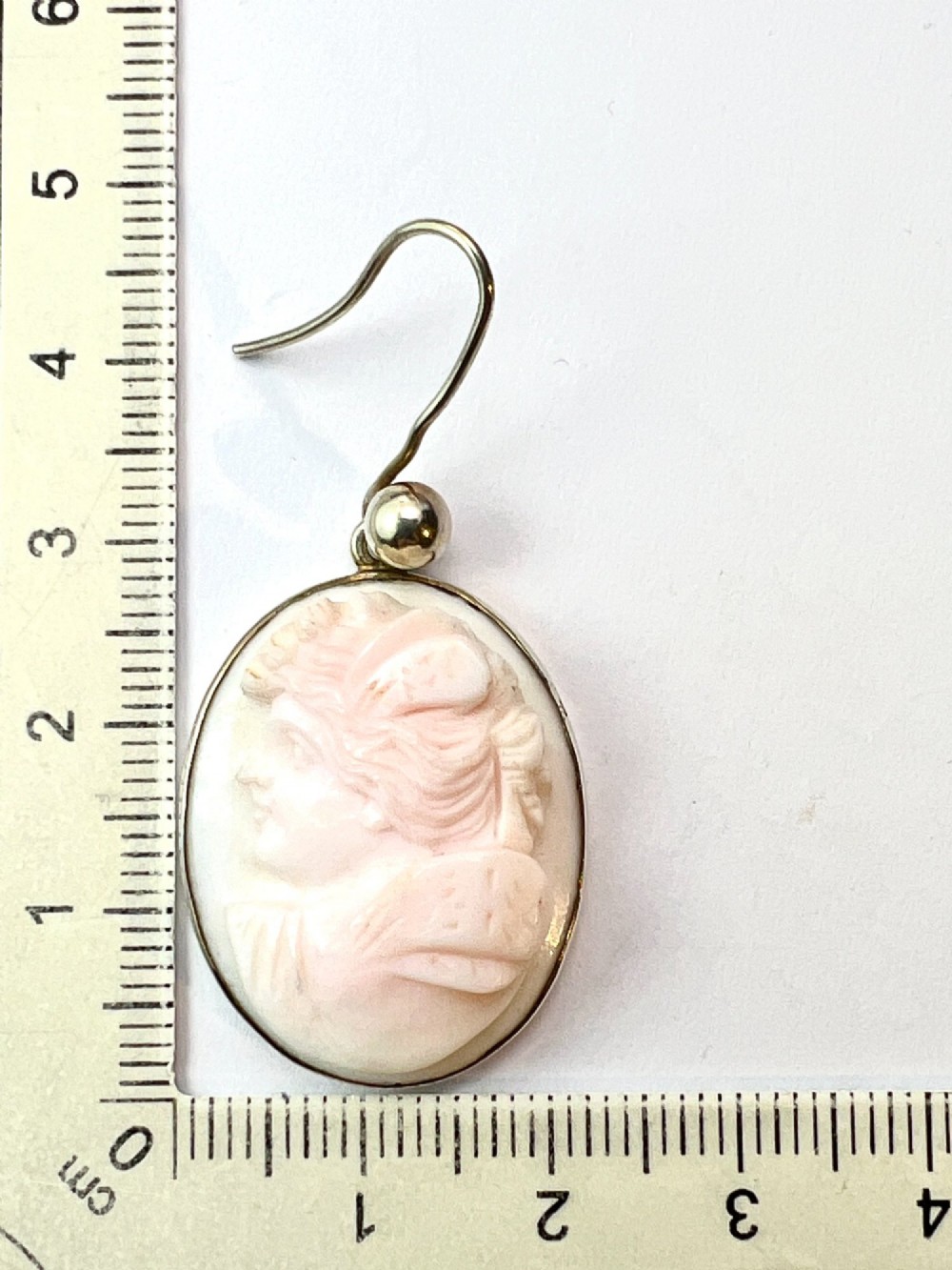 A pair of oval drop earrings featuring carved pink and white queen conch shell cameos depicting classical profile portraits set in silver mounts. View VII