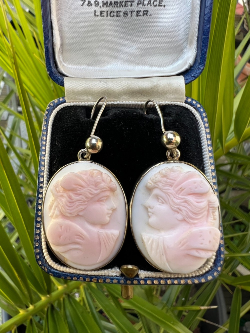 A pair of oval drop earrings featuring carved pink and white queen conch shell cameos depicting classical profile portraits set in silver mounts. View VIII