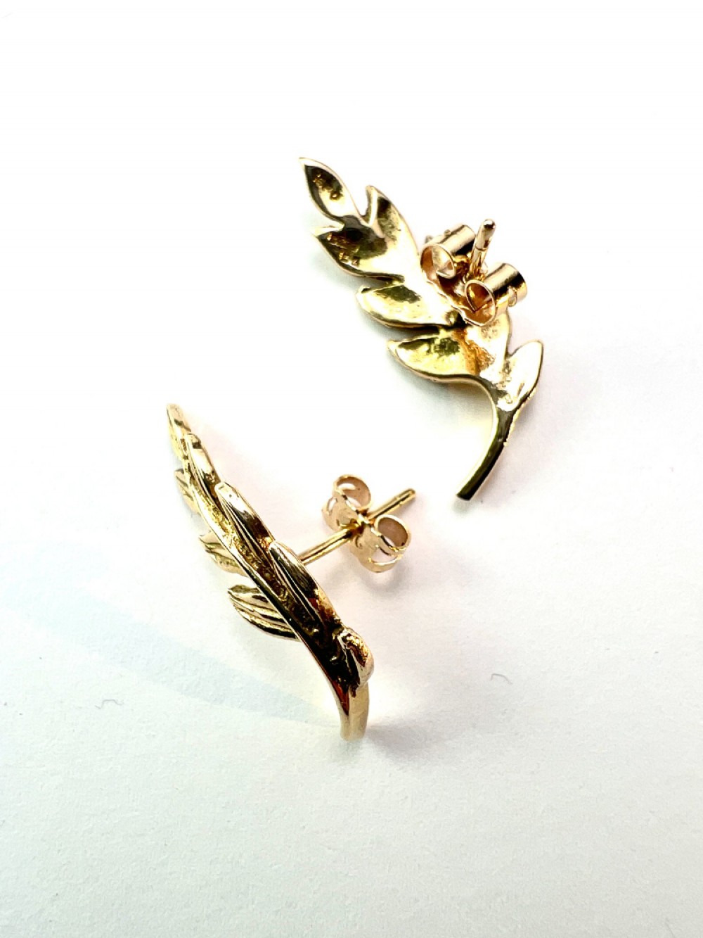 A pair of 9ct yellow gold stud earrings crafted in the shape of curved laurel leaf branches with textured vein details. View VI