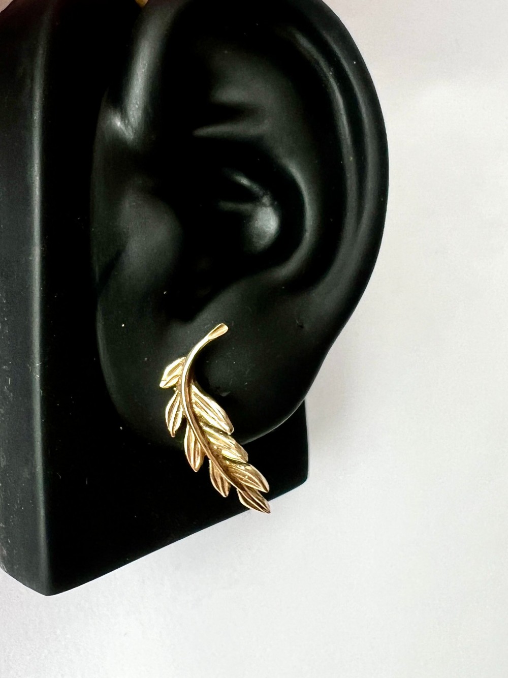 A pair of 9ct yellow gold stud earrings crafted in the shape of curved laurel leaf branches with textured vein details. View X