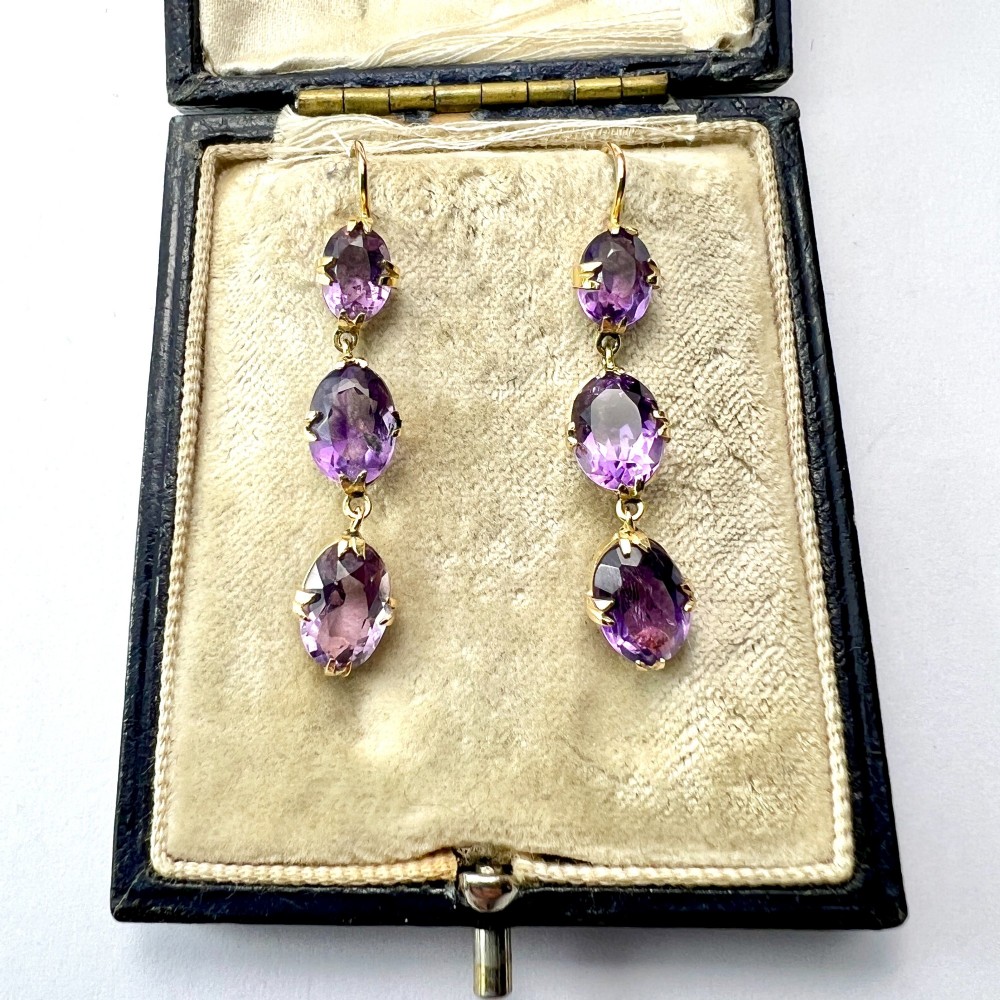 A pair of antique 9ct yellow gold drop earrings, each set with three articulated oval faceted purple amethysts in claw mounts.