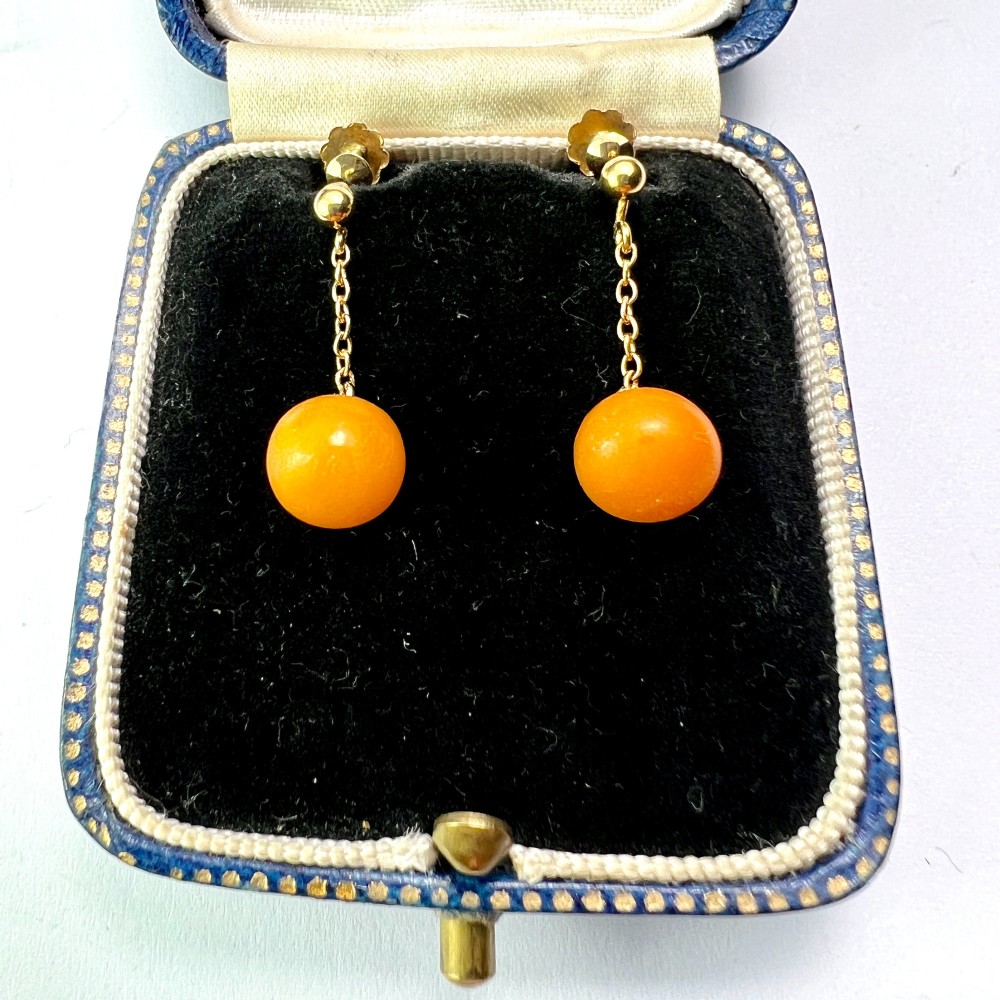 A pair of Edwardian 9ct gold drop earrings featuring spherical amber beads suspended from fine link chains.