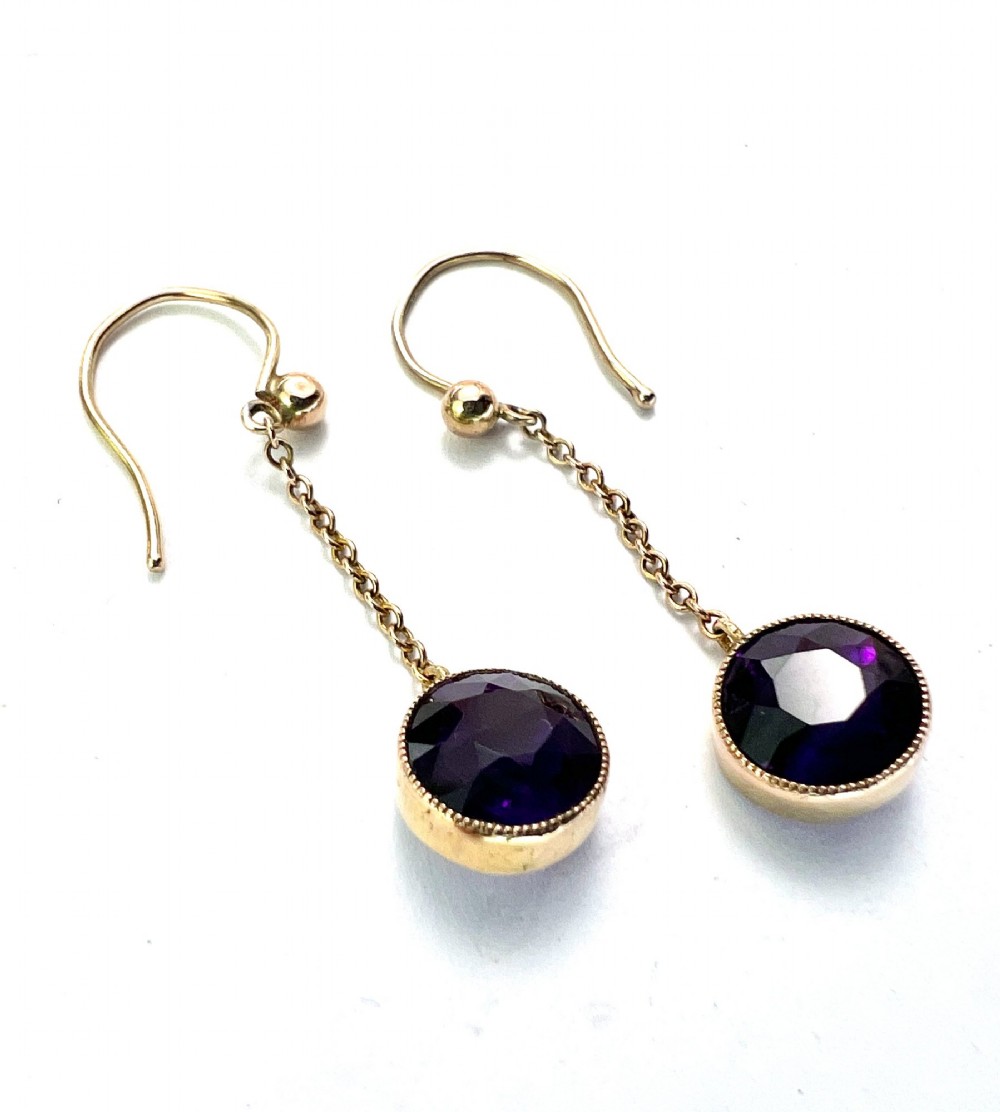 A pair of Edwardian 9ct yellow gold drop earrings featuring round, bezel-set faceted purple amethysts suspended from fine link chains. View VI