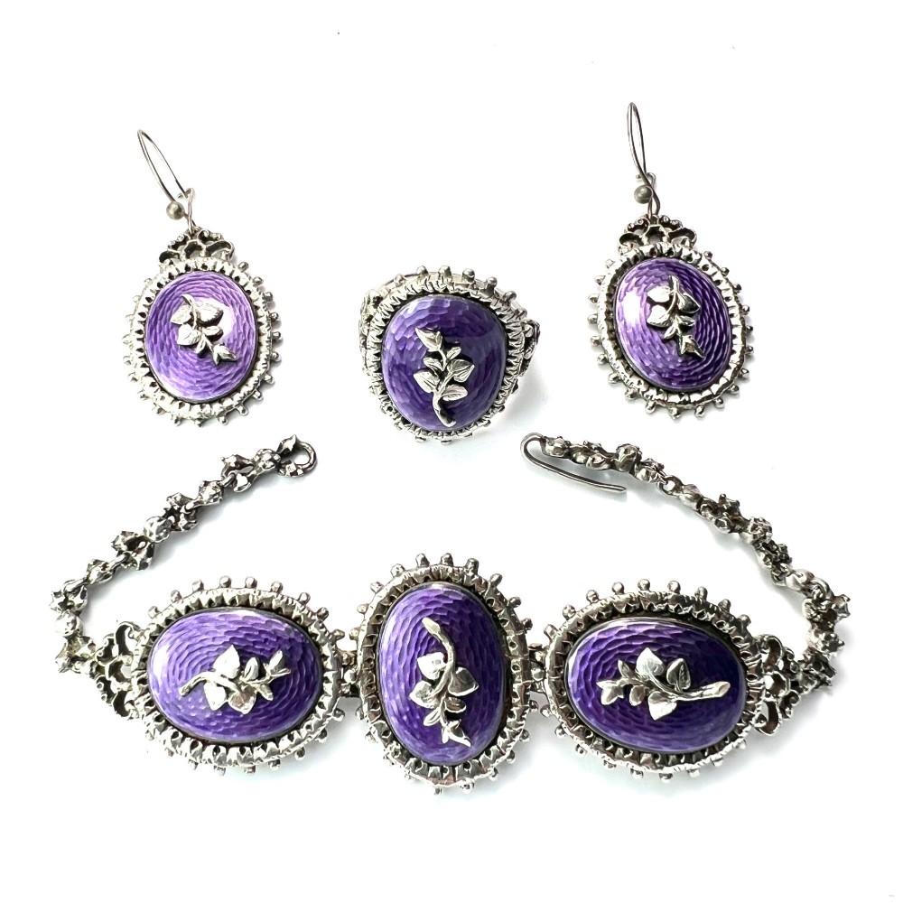 A matching silver jewellery set featuring purple guilloche enamel panels decorated with silver leaf motifs, including drop earrings, a ring, and an articulated link bracelet.