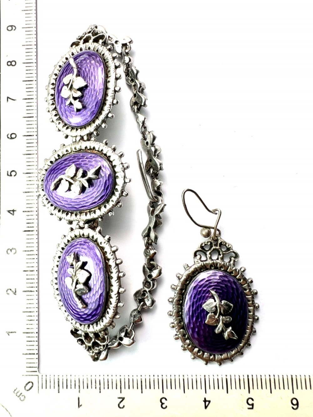 A matching silver jewellery set featuring purple guilloche enamel panels decorated with silver leaf motifs, including drop earrings, a ring, and an articulated link bracelet. View X