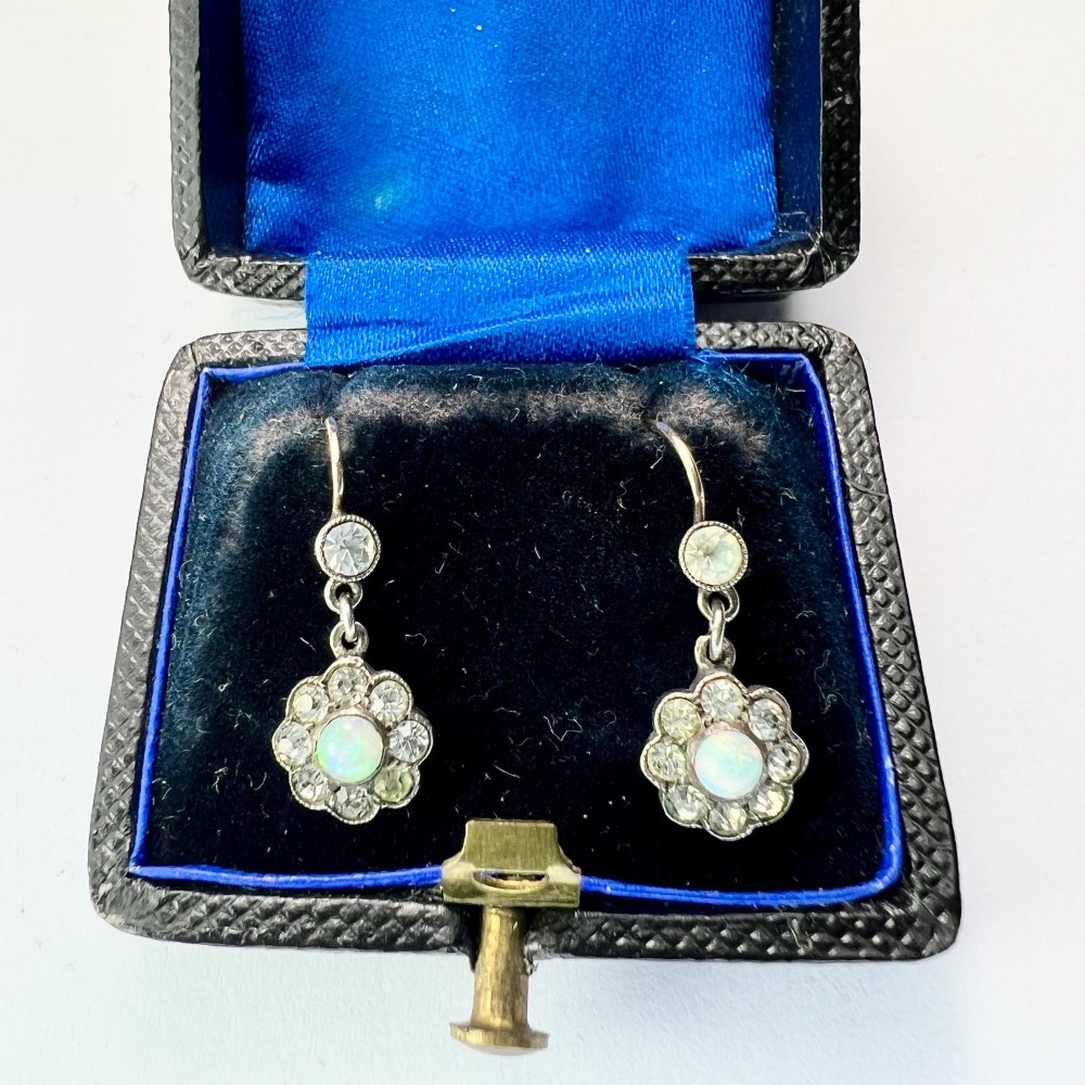 A pair of antique silver drop earrings featuring central opals surrounded by sparkling paste stones in floral cluster settings.