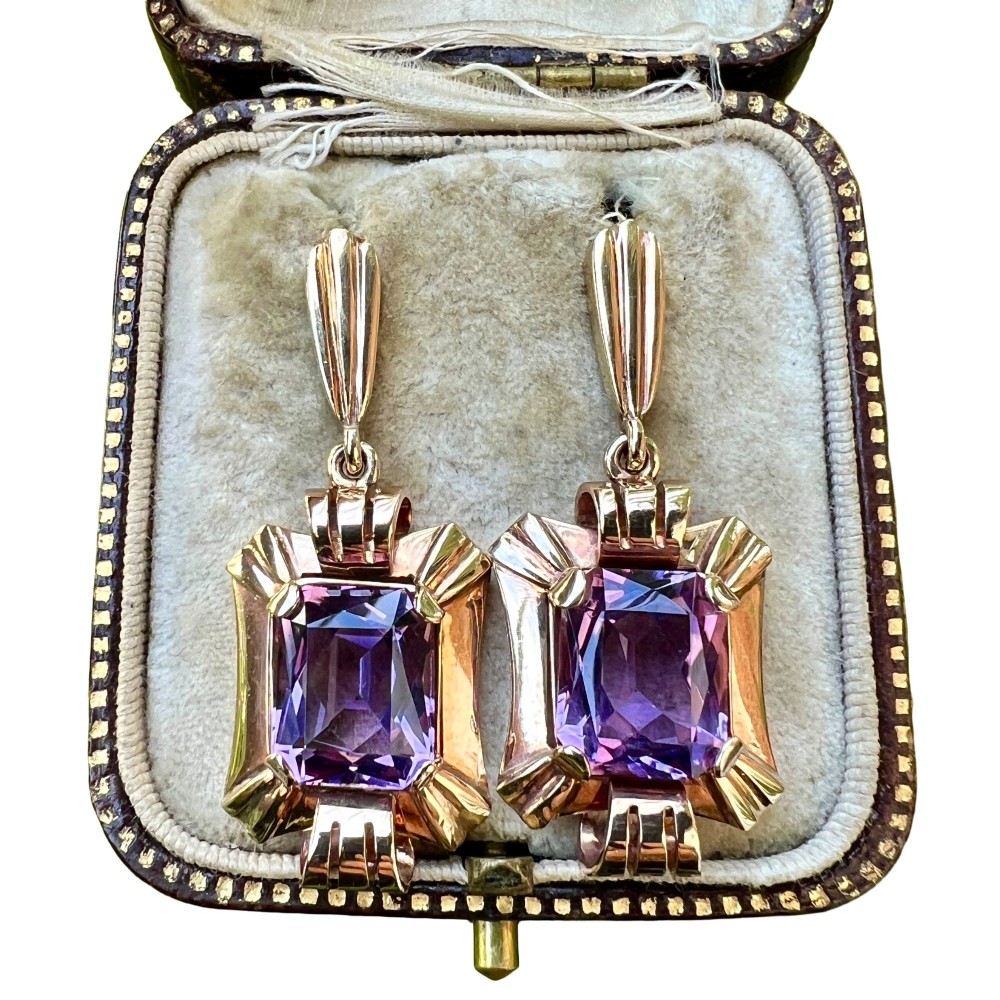 A pair of late Art Deco gold drop earrings featuring rectangular emerald-cut purple amethyst stones set within fluted geometric mounts.