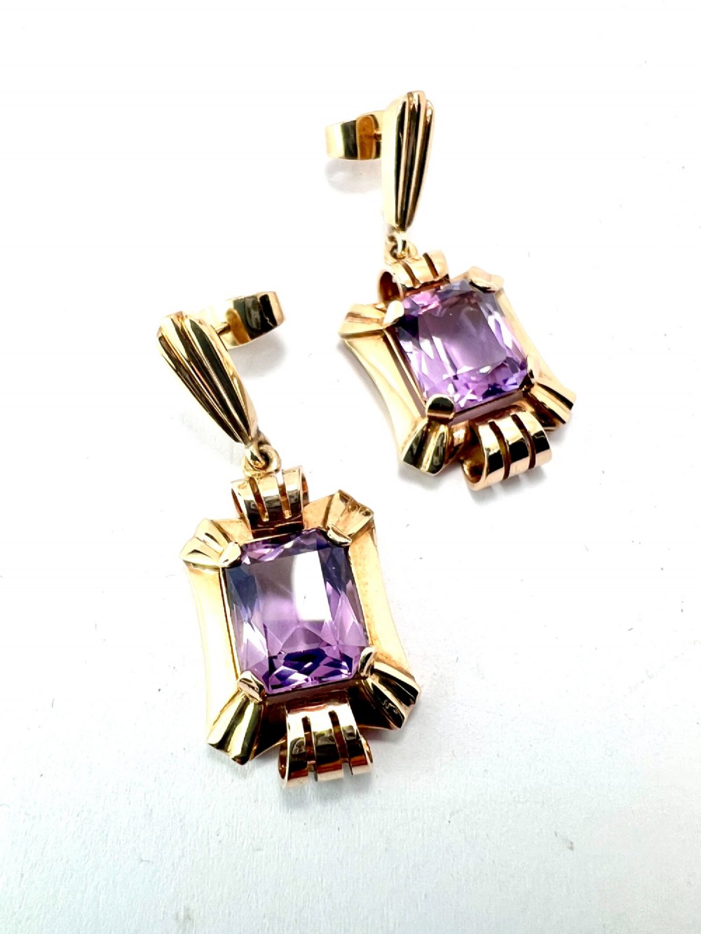 A pair of late Art Deco gold drop earrings featuring rectangular emerald-cut purple amethyst stones set within fluted geometric mounts. View V