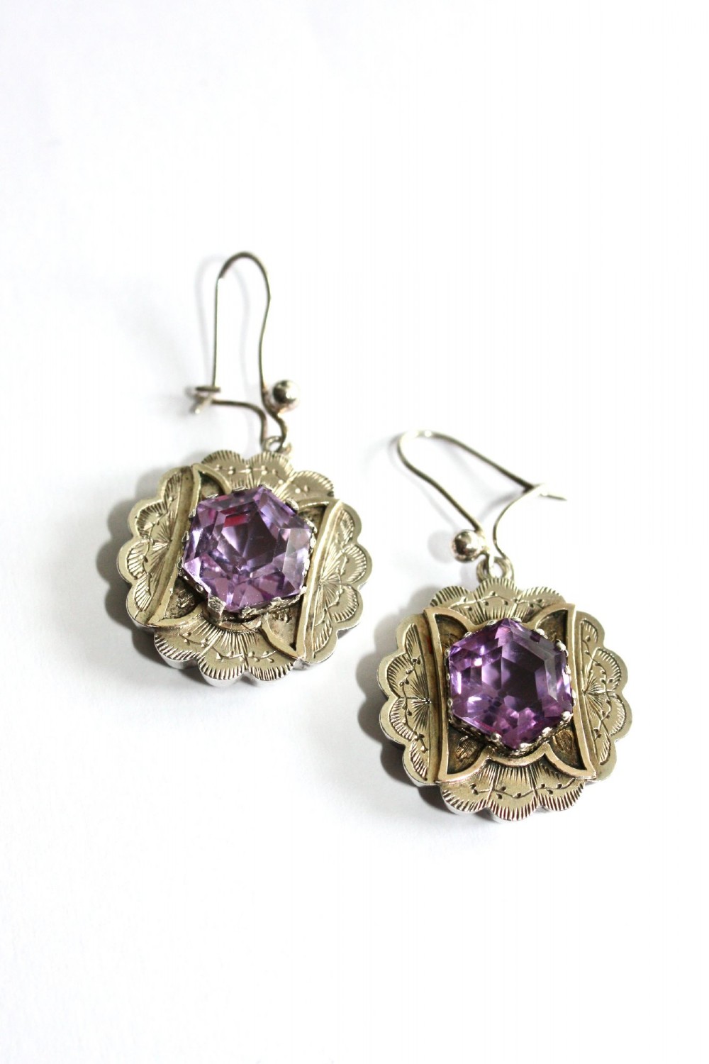 A Victorian silver jewellery set comprising a circular brooch and matching drop earrings, each featuring engraved detailing and a central faceted purple amethyst stone. View II