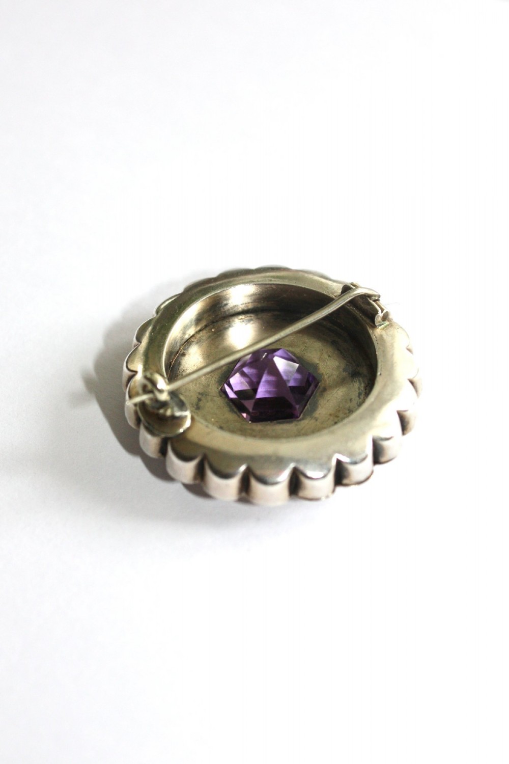 A Victorian silver jewellery set comprising a circular brooch and matching drop earrings, each featuring engraved detailing and a central faceted purple amethyst stone. View III