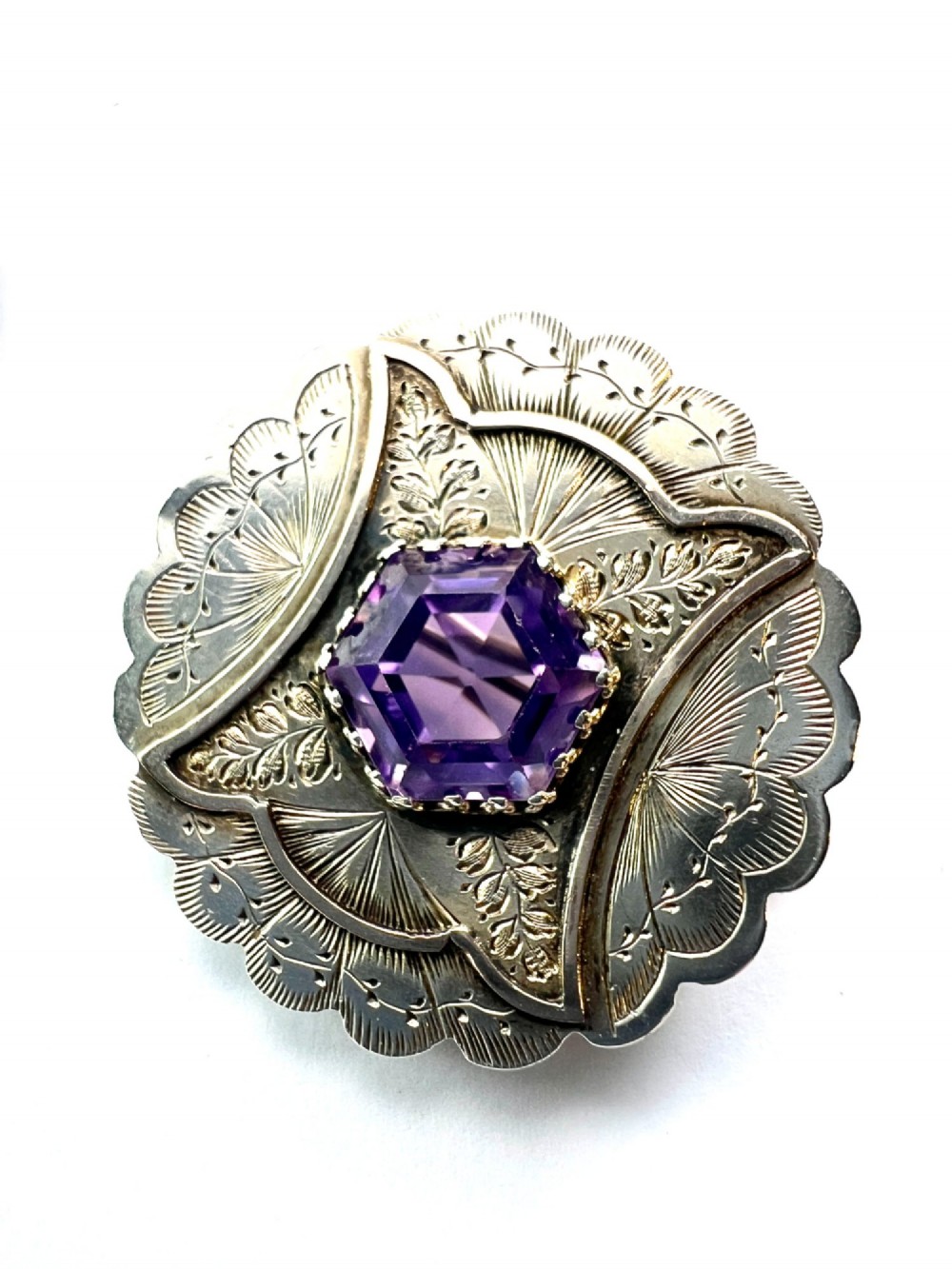 A Victorian silver jewellery set comprising a circular brooch and matching drop earrings, each featuring engraved detailing and a central faceted purple amethyst stone. View V