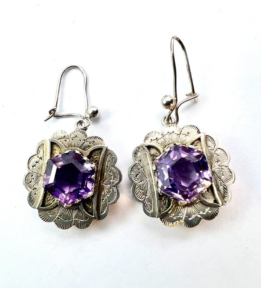A Victorian silver jewellery set comprising a circular brooch and matching drop earrings, each featuring engraved detailing and a central faceted purple amethyst stone. View VI