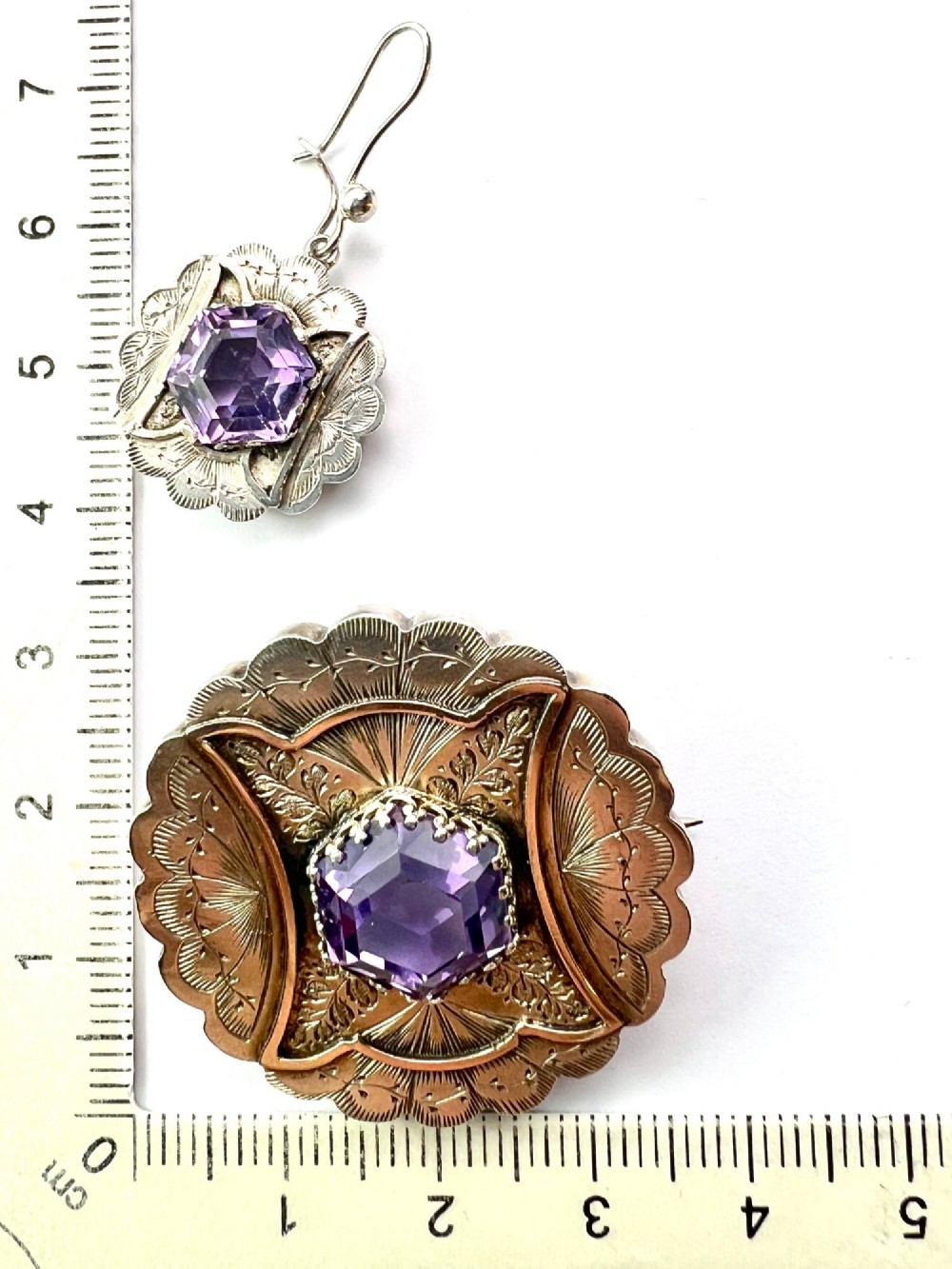 A Victorian silver jewellery set comprising a circular brooch and matching drop earrings, each featuring engraved detailing and a central faceted purple amethyst stone. View VII
