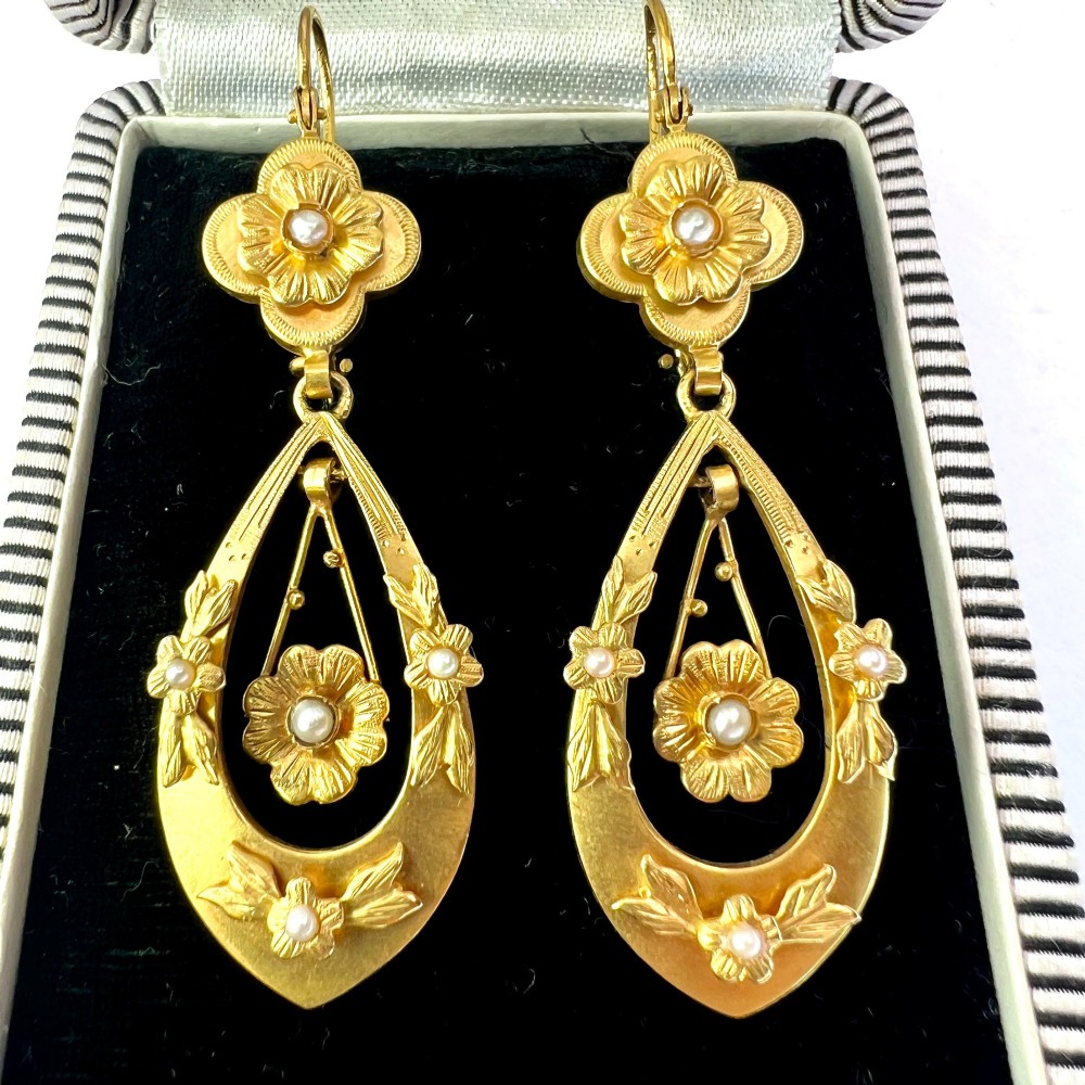 A pair of late Victorian yellow gold drop earrings featuring floral detailing and central pearl settings.