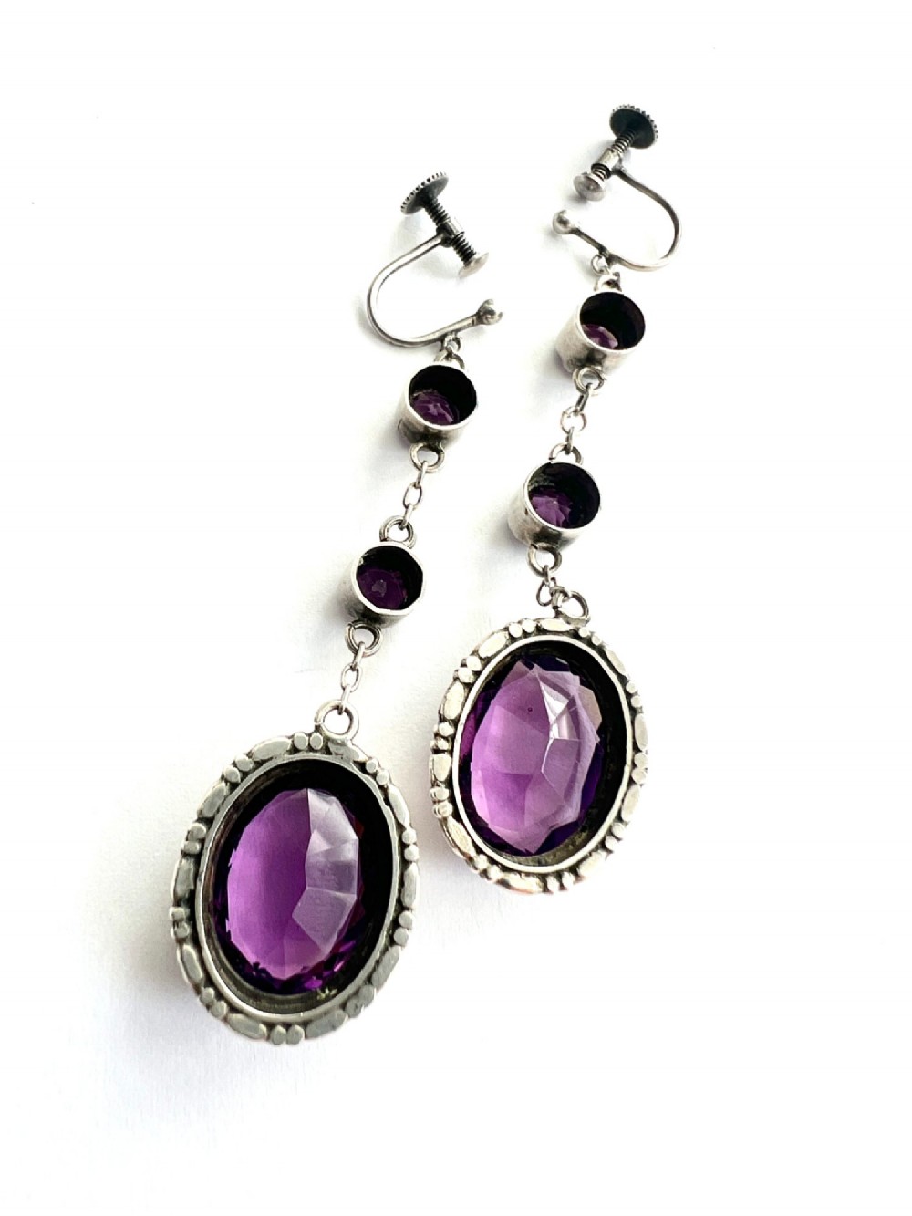 A pair of Art Deco drop earrings featuring faceted purple paste stones set in silver with screwback mechanisms. View II