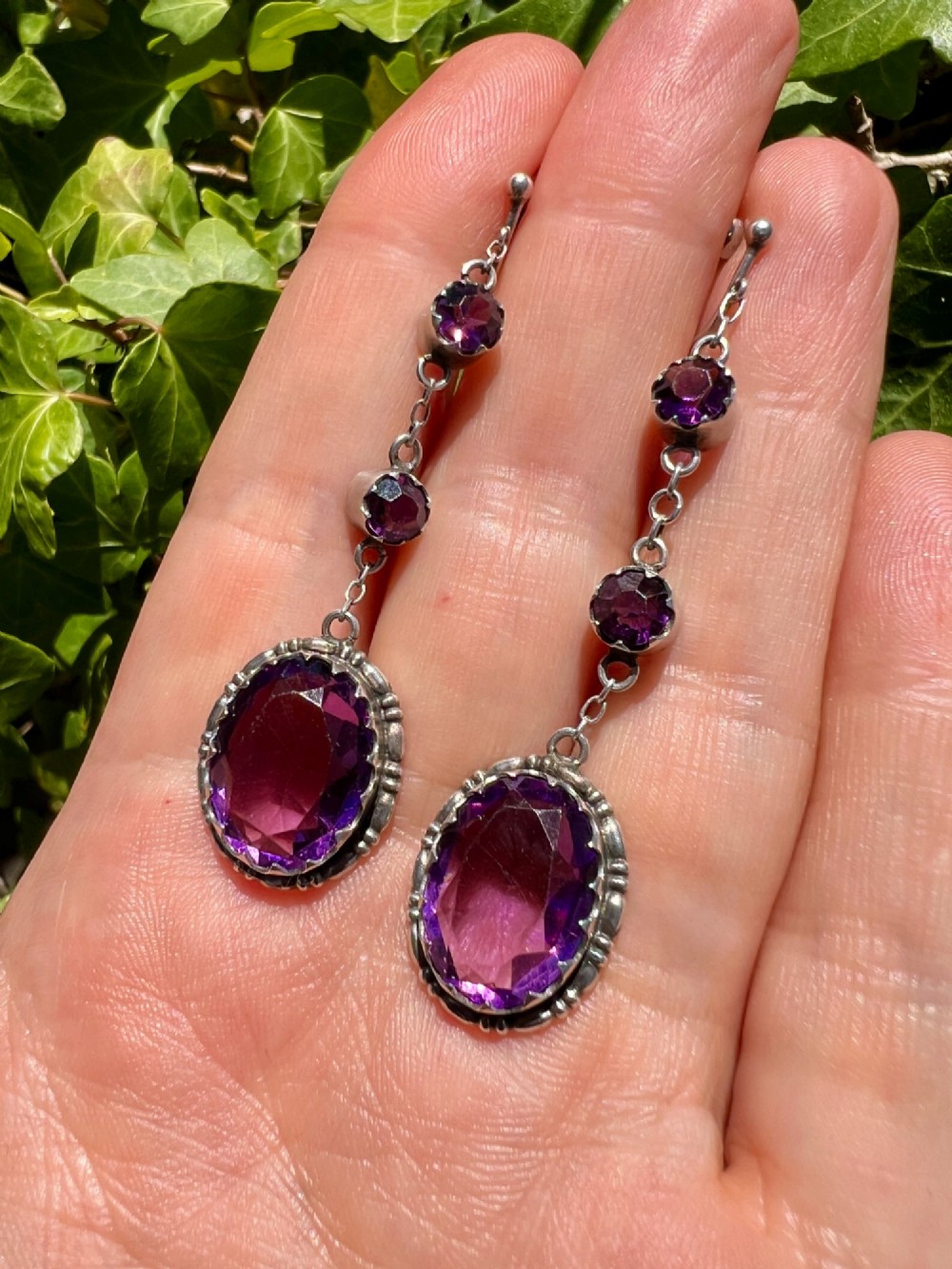 A pair of Art Deco drop earrings featuring faceted purple paste stones set in silver with screwback mechanisms. View IV