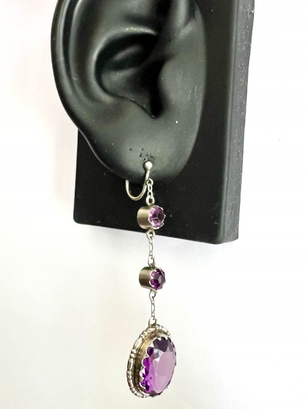 A pair of Art Deco drop earrings featuring faceted purple paste stones set in silver with screwback mechanisms. View V