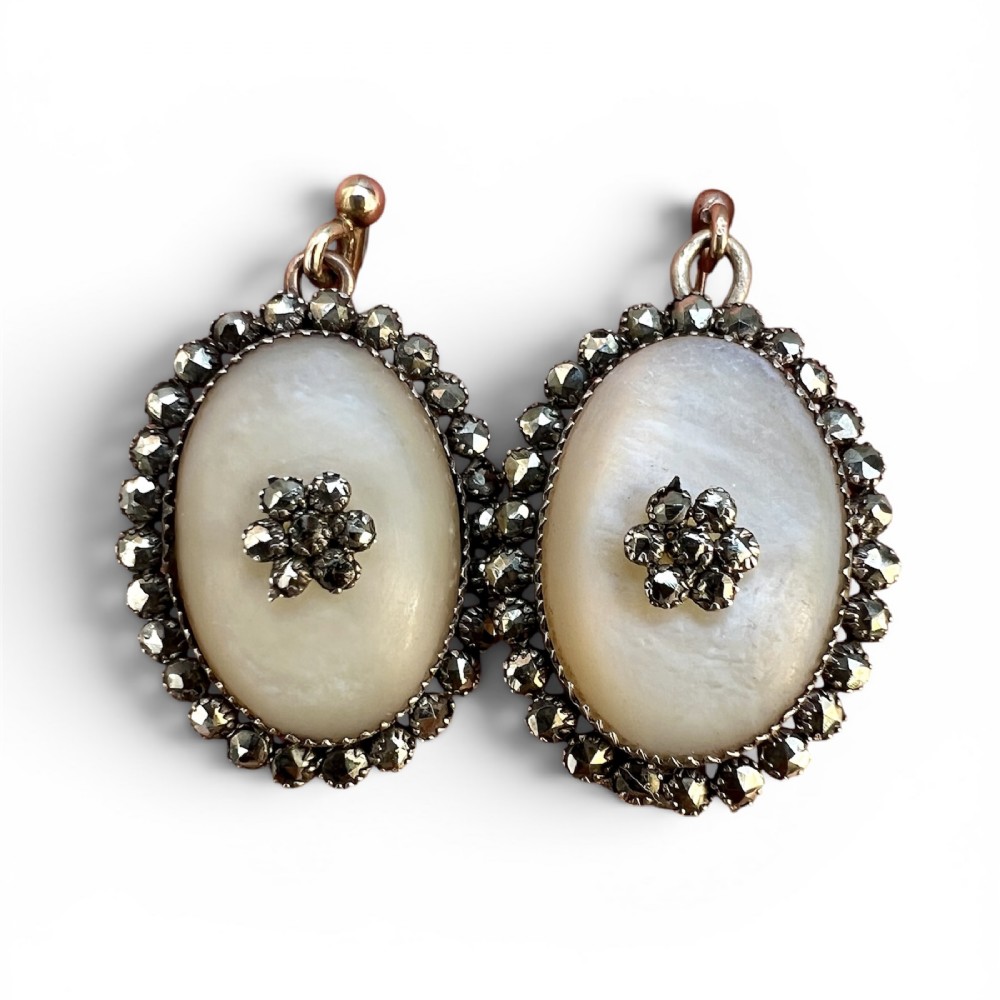 A pair of oval Georgian drop earrings featuring mother of pearl cabochons framed by faceted marcasite stones with a central marcasite floral cluster.
