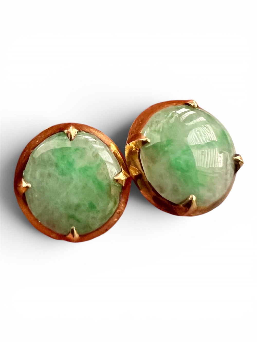 A pair of circular pale green jadeite cabochon stud earrings held in yellow gold claw settings.