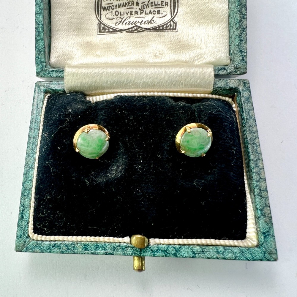 A pair of circular pale green jadeite cabochon stud earrings held in yellow gold claw settings. View IV
