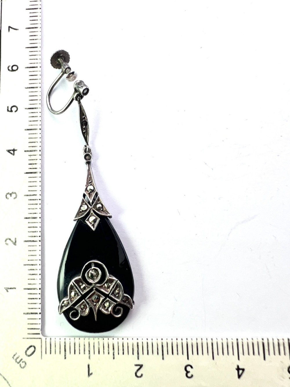 A pair of Art Deco drop earrings featuring polished teardrop-shaped black onyx stones suspended beneath decorative silver mounts set with marcasite stones. View VI