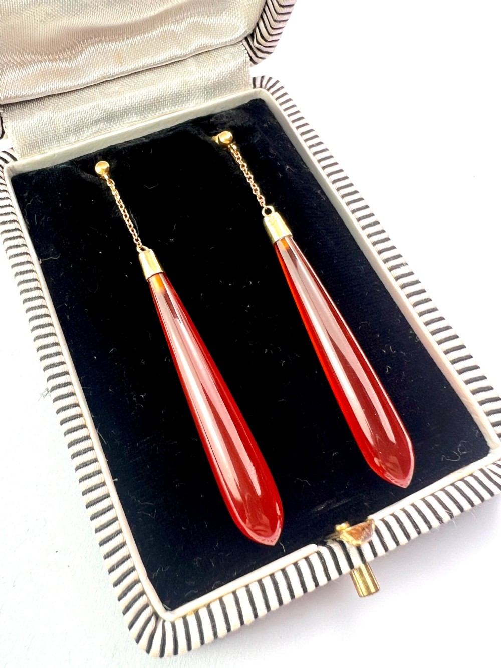 A pair of antique Edwardian drop earrings featuring long, polished teardrop-shaped carnelian stones suspended from delicate 9ct gold chains. View II