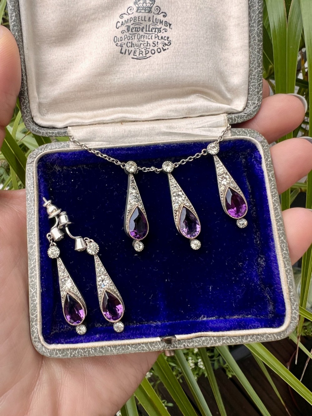 An Art Deco jewellery set featuring a silver chain necklace with teardrop purple paste drops and matching drop earrings. View VII