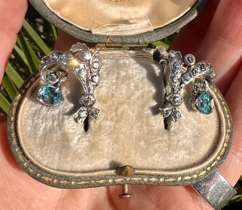 Pair of Edwardian silver screwback drop earrings featuring scrollwork set with clear paste stones and suspended light blue glass gems. View VI
