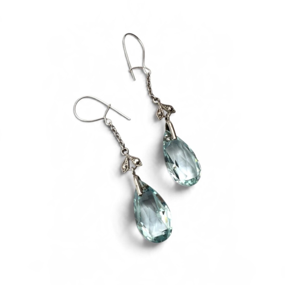 A pair of Edwardian silver drop earrings featuring faceted teardrop-shaped light blue paste stones hanging from delicate chains. View IV