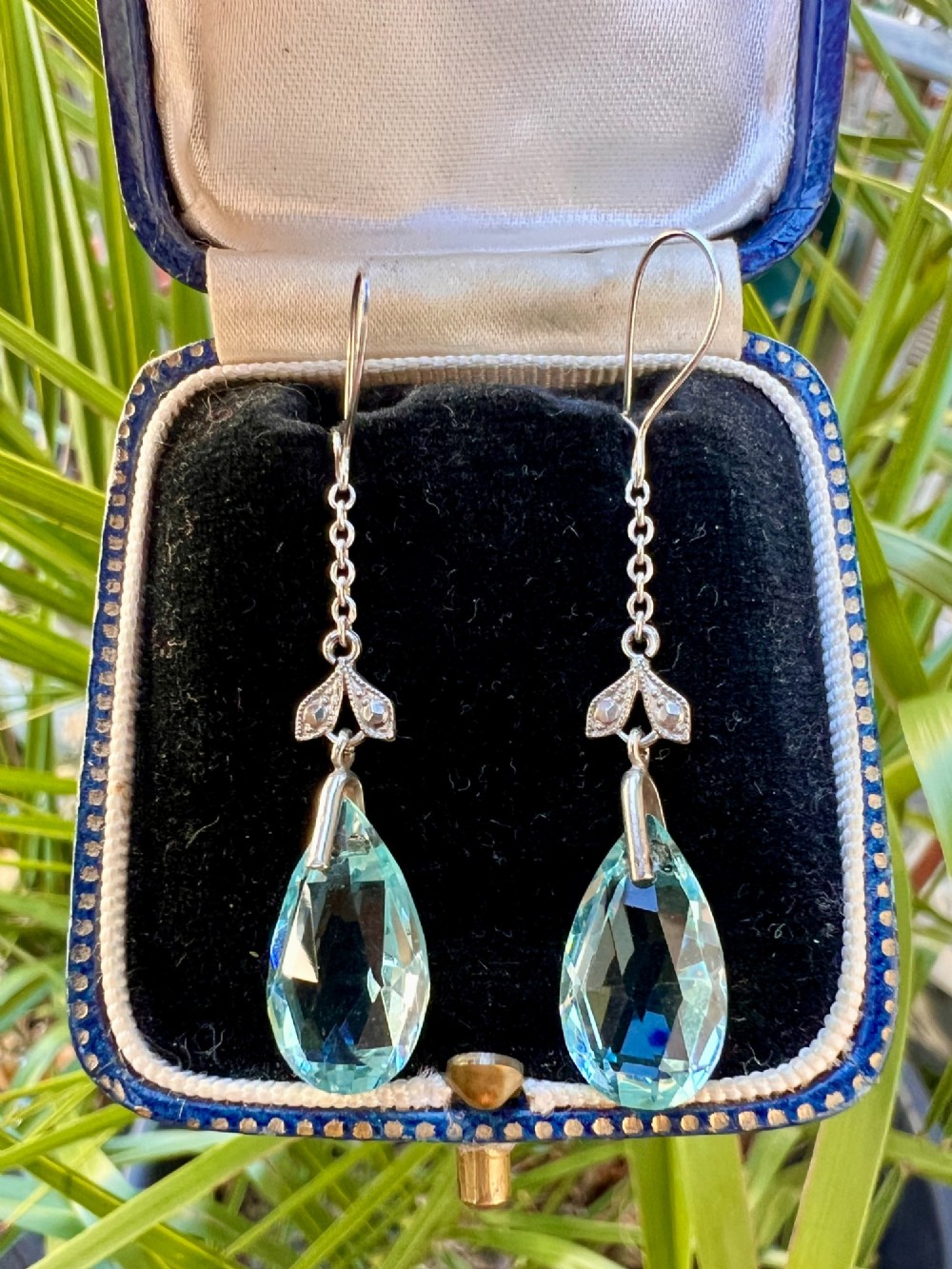 A pair of Edwardian silver drop earrings featuring faceted teardrop-shaped light blue paste stones hanging from delicate chains. View VI
