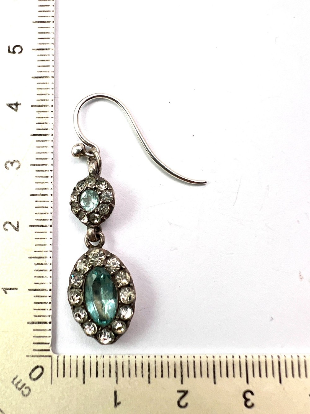 A pair of antique silver drop earrings featuring oval light blue paste central stones surrounded by clear paste halos suspended from wire hooks. View VI