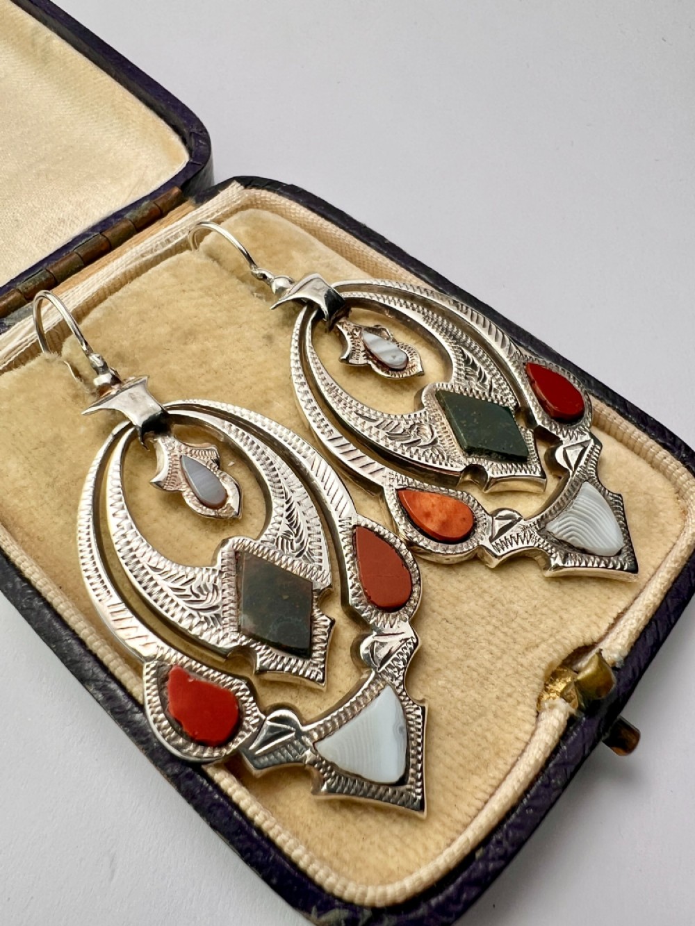 A pair of Victorian sterling silver drop pendant earrings featuring hand-engraved openwork panels inlaid with geometric red jasper, green moss agate, and grey banded agate stones. View III