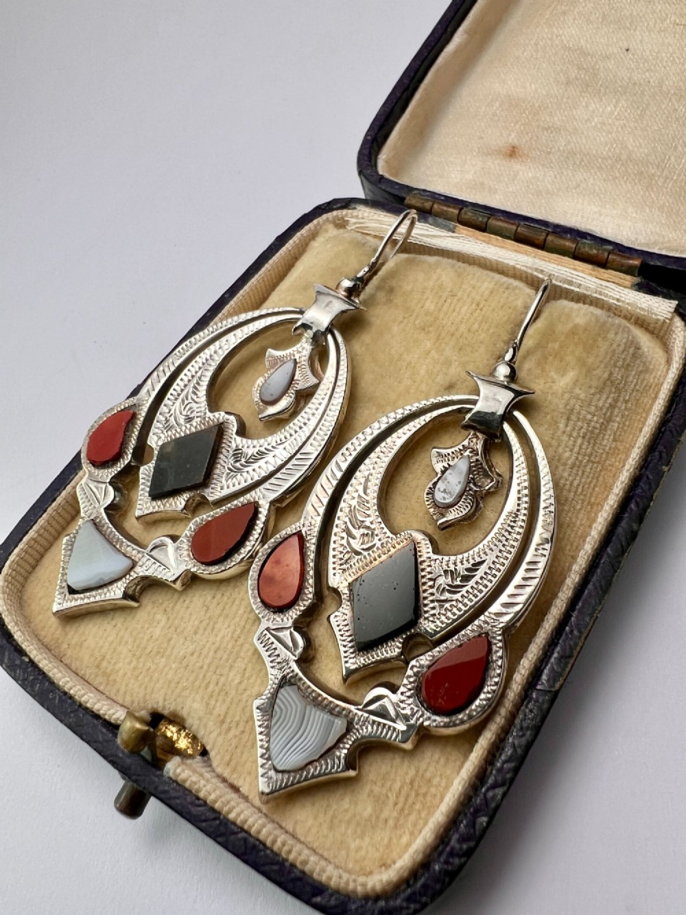 A pair of Victorian sterling silver drop pendant earrings featuring hand-engraved openwork panels inlaid with geometric red jasper, green moss agate, and grey banded agate stones. View IV