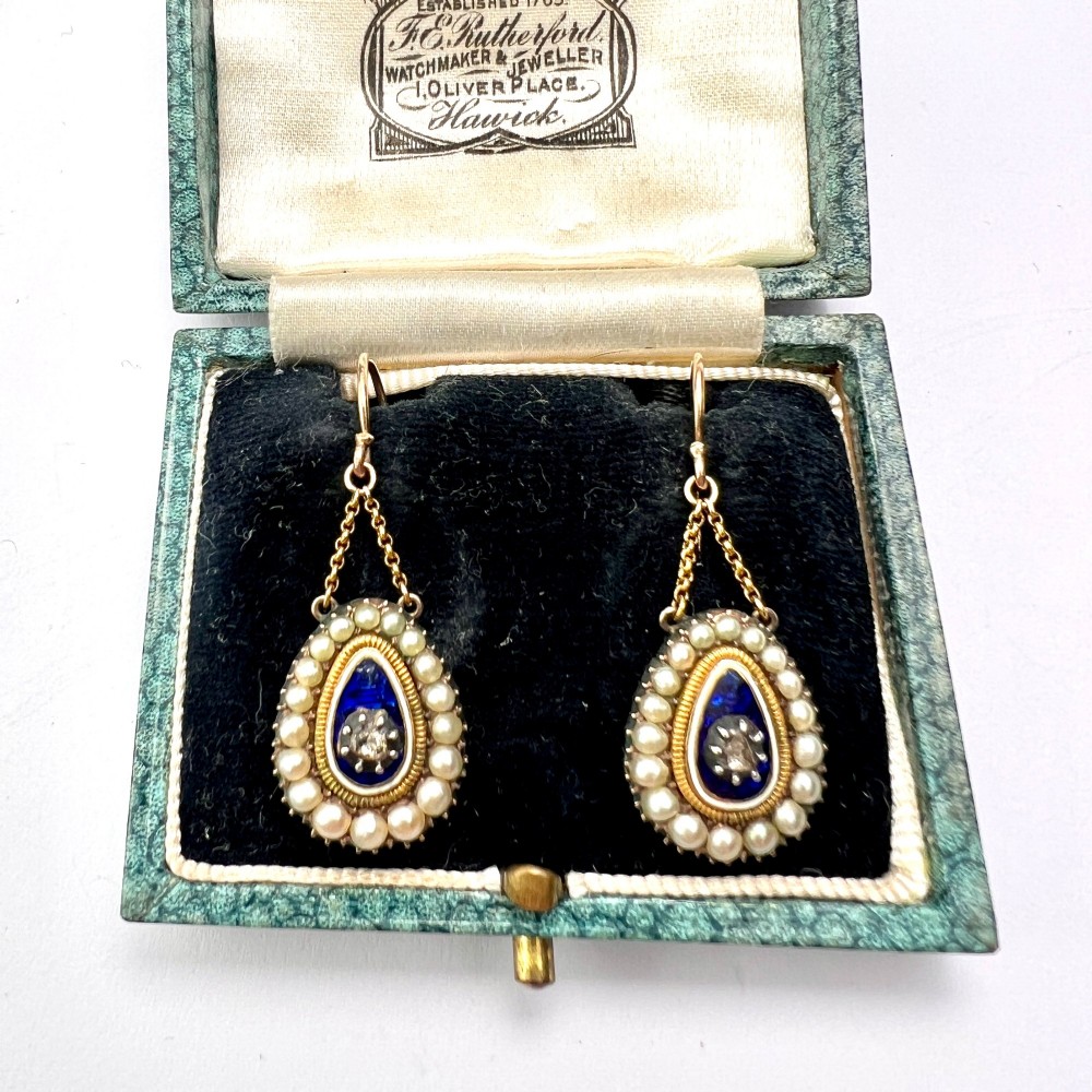 A pair of antique Georgian drop earrings featuring a central diamond set within blue enamel, bordered by seed pearls and suspended from fine gold chains. View VII
