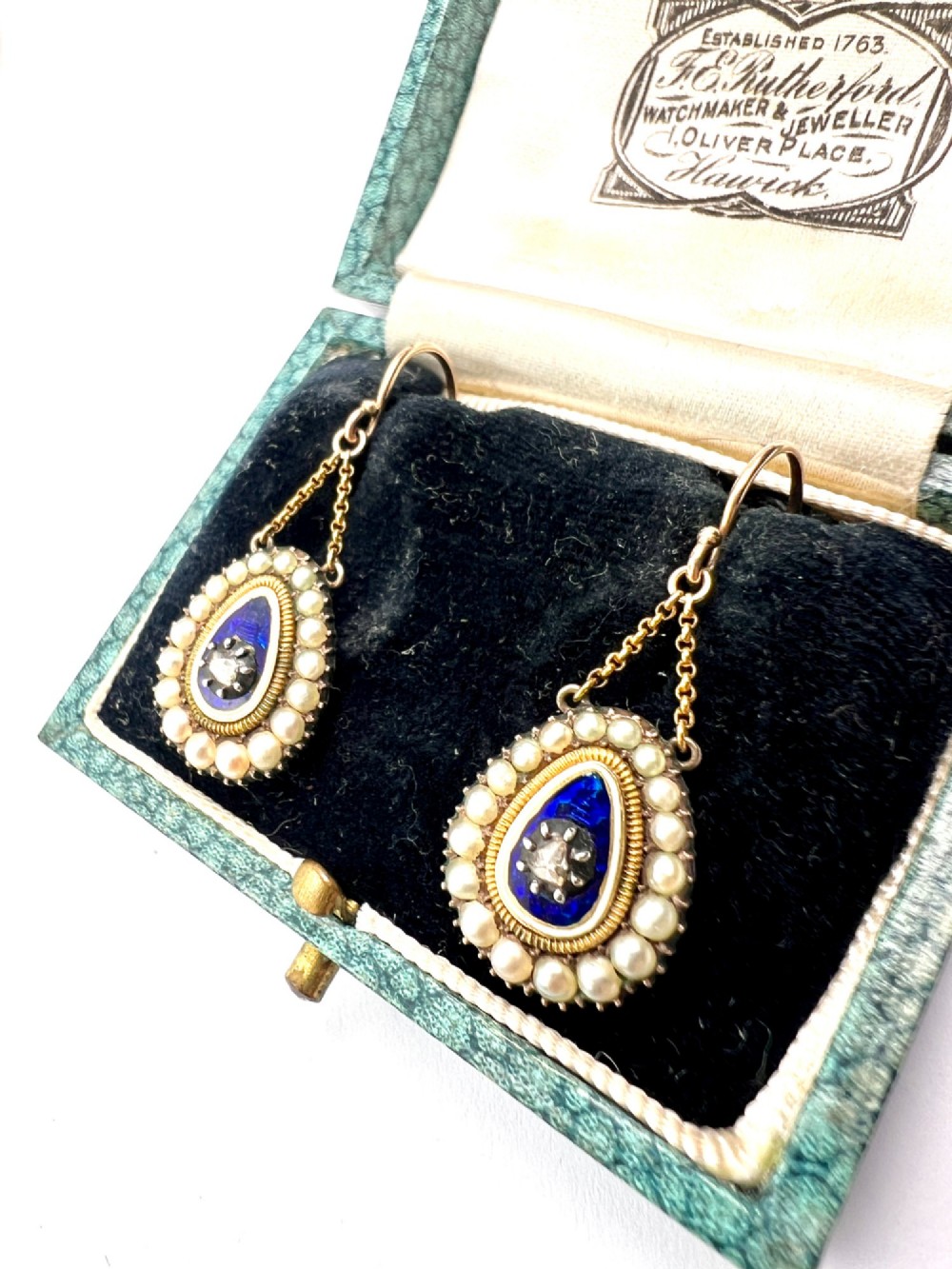A pair of antique Georgian drop earrings featuring a central diamond set within blue enamel, bordered by seed pearls and suspended from fine gold chains. View VIII