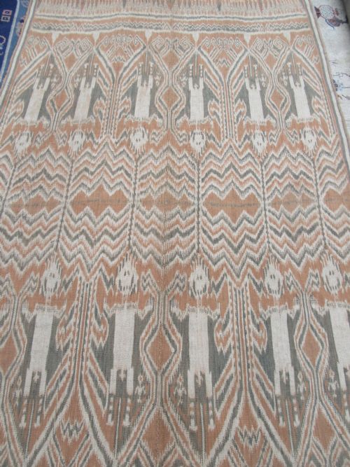 fig 2. A large handwoven antique ikat textile panel from Borneo displaying vertical rows of stylised human figures and chevron patterning in terracotta brown, cream, and grey.