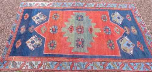 fig 1. A large hand-knotted antique Caucasian Kazak rug featuring a central stepped green medallion set within a terracotta red and navy blue geometric field.