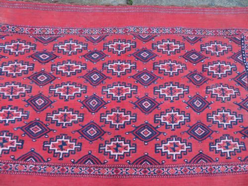 fig 1. Mid-nineteenth century Turkmen chuval textile featuring repeated geometric gul medallions woven in navy blue and ivory against a crimson red field with a flat-woven lower section.