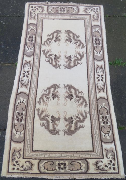 fig 1. A rectangular hand-knotted cream wool rug featuring two central dragon medallions, a key meander border, and grey decorative motifs.