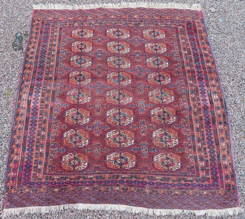 fig 1. An antique Tekke Turkmen hand-knotted wool rug featuring repeating geometric gul patterns across a deep red field framed by multiple ornamental borders.