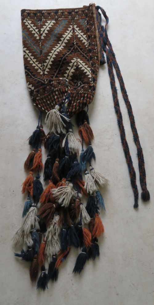 fig 1. A hand-woven Yomut Turkmen Ok Bash tent-pole bag featuring geometric chevron patterns in rust brown, indigo, and cream wool, finished with braided ties and multi-coloured tassels.