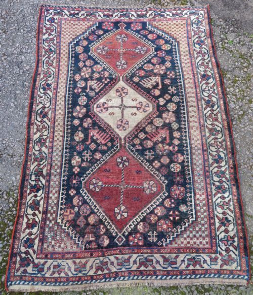 fig 1. An antique hand-knotted Persian tribal rug featuring three central diamond-shaped medallions, geometric peacock motifs, and multi-layered borders in navy blue, red, and ivory wool.