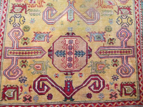 fig 2. An antique hand-knotted Caucasian rug featuring a distressed yellow central field patterned with geometric ram horn motifs framed by red and green decorative borders.