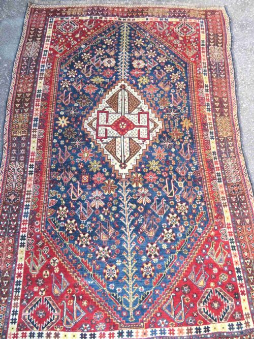 fig 1. An antique Qashqai tribal wool rug featuring a deep blue central field with geometric bird motifs, red spandrels, and a complex multi-band border.