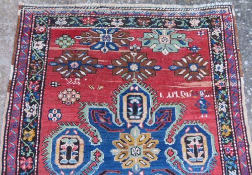 fig 1. An antique Caucasian Karabagh handwoven wool rug featuring blue and black central geometric medallions on a red field with floral borders.