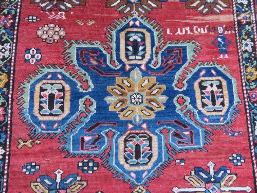 fig 2. An antique Caucasian Karabagh handwoven wool rug featuring blue and black central geometric medallions on a red field with floral borders.