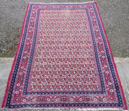 fig 1. An antique Persian Meshed Doroksh wool rug featuring a repeating all-over boteh pattern on a cream field within multi-banded crimson and navy borders.